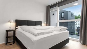 Een moderne slaapkamer met een groot bed, twee bedlampen en uitzicht op een gebouw door een groot raam.