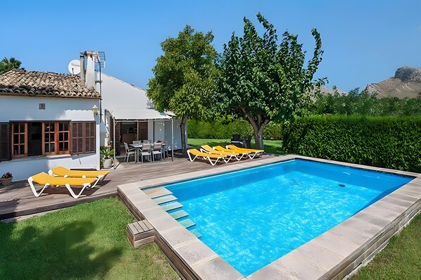A rectangular swimming pool with a tiled deck, surrounded by a white building with a tiled roof, and a tree in the background. - Villa Provenza with Private Pool, Terrace, A/C & Wi-Fi (Las Palmeras)