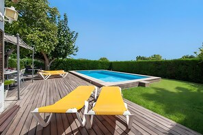 Eine Holzterrasse mit zwei gelben Liegestühlen, einem Pool und einem gepflegten Rasen.