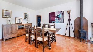 A dining area with a wooden table and chairs, a cabinet, a painting, and a wood-burning stove. - Villa Provenza with Private Pool, Terrace, A/C & Wi-Fi (Las Palmeras)