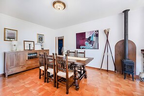 Ein Essbereich mit Holztisch und -stühlen, einem Schrank, einem Gemälde und einem Kaminofen.