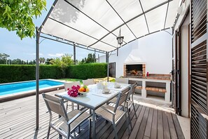Ein überdachter Essbereich im Freien mit Pool, Grill und Blick ins Grüne.