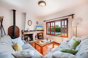 A cozy living room with a fireplace, a sofa set, a coffee table, and a large window with curtains. - Villa Provenza with Private Pool, Terrace, A/C & Wi-Fi (Las Palmeras)
