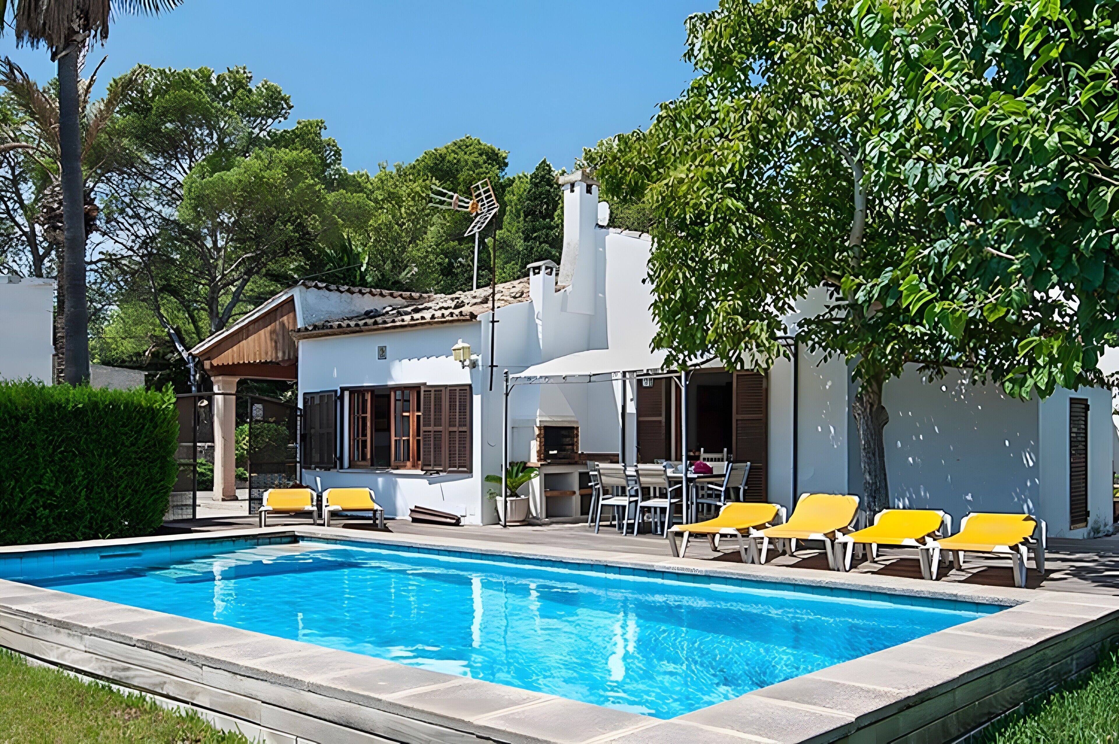 Una piscina con sillas de descanso, un patio y un edificio con fachada blanca.