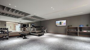 Een sportschool met trainingsapparatuur, een spiegel en een wandgemonteerd scherm.