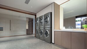 A modern laundry room with four stacked washing machines, a large mirror, and a countertop with a sink and plants.