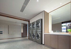 A modern laundry room with four stacked washing machines, a large mirror, and a countertop with a sink and plants. - Atour Hotel MayFourthSquare MixC Qingdao (Qingdao)