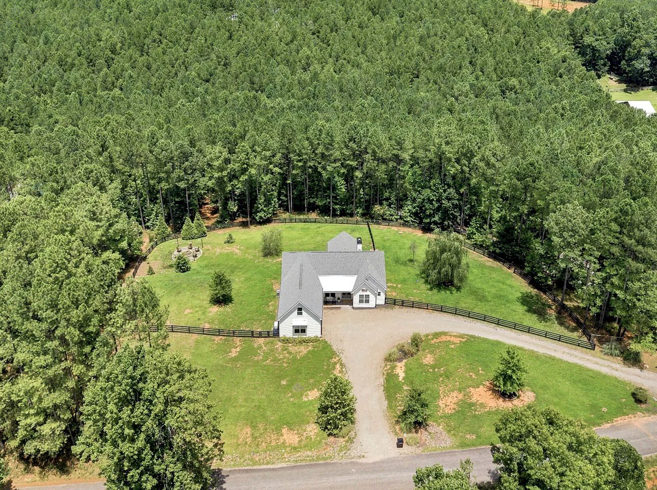Une grande maison de plain-pied, dotée d’une cour clôturée et entourée d’une forêt dense.