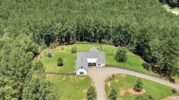 Une grande maison de plain-pied, dotée d’une cour clôturée et entourée d’une forêt dense.