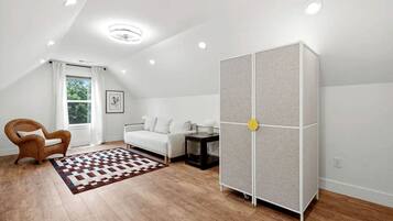 Une pièce moderne avec un canapé blanc, une chaise en bois, un tapis à motifs et un grand meuble doté d’une poignée ronde.