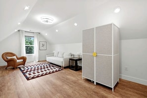 A modern room with a white sofa, a wooden chair, a patterned rug, and a tall cabinet with a circular handle.