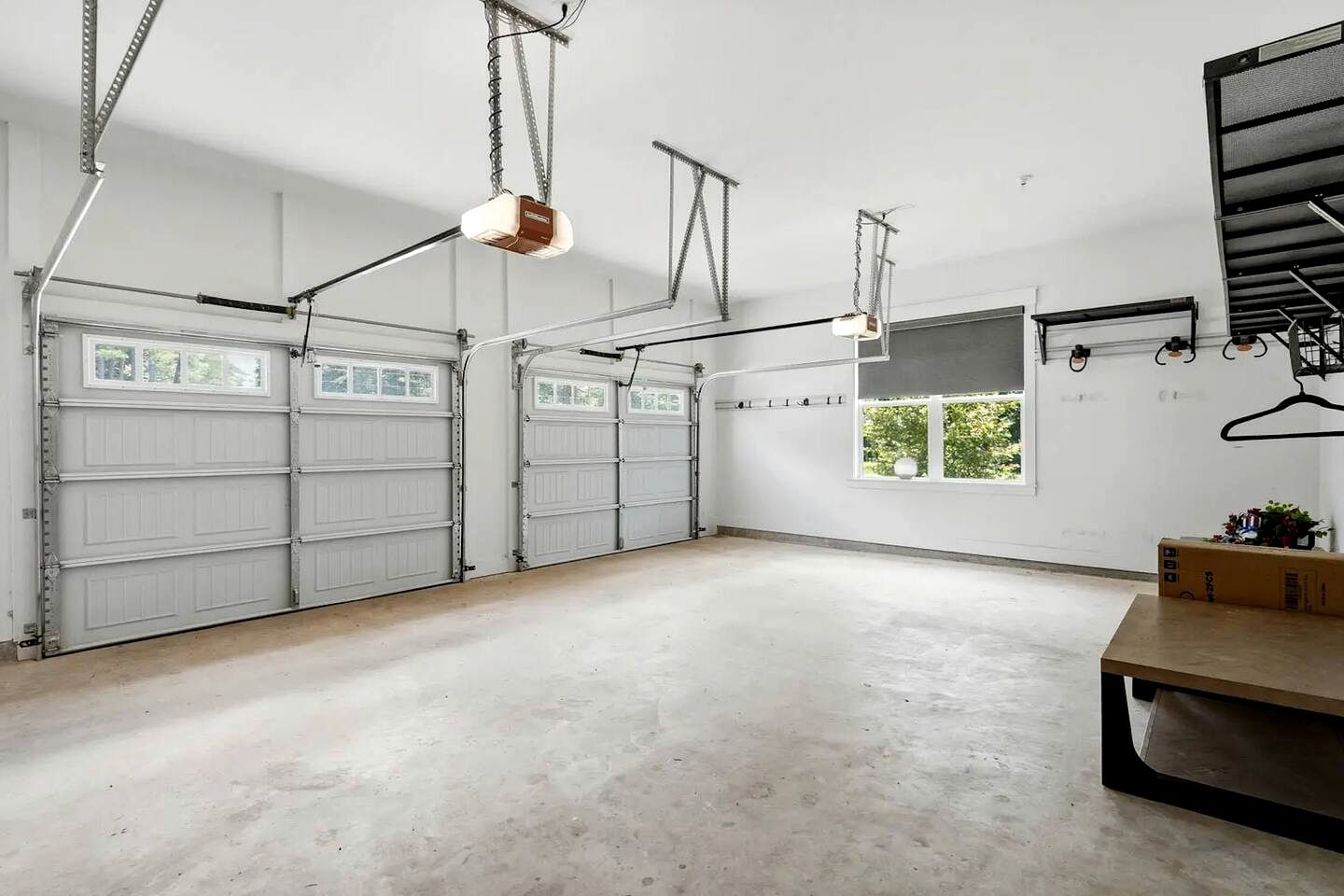 A spacious garage with two white garage doors, a concrete floor, and a hanging light fixture.