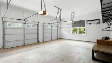 A spacious garage with two white garage doors, a concrete floor, and a hanging light fixture.