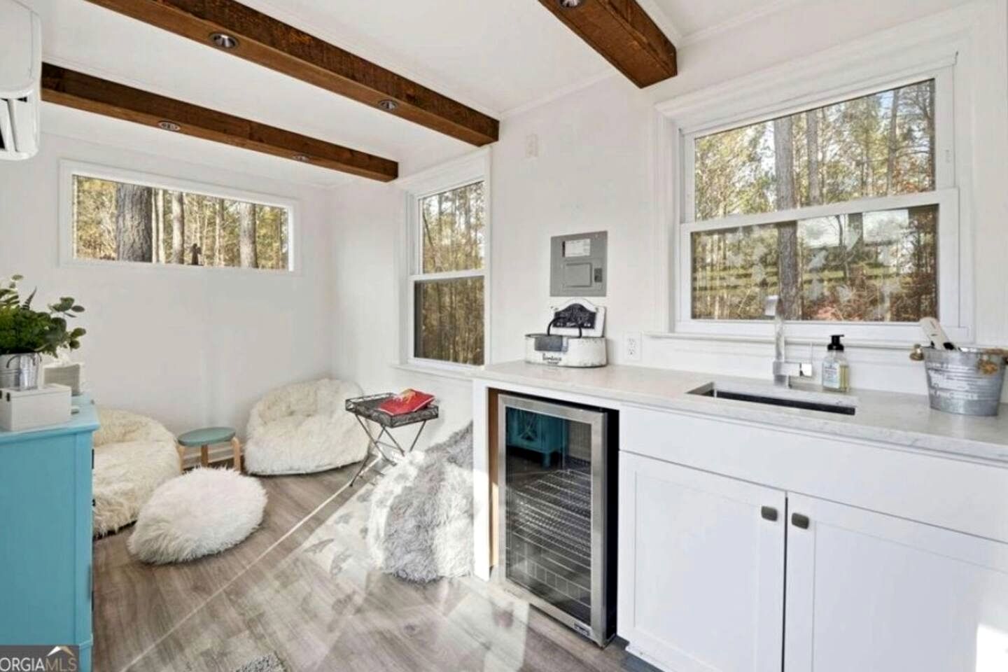 Une cuisine moderne avec des meubles blancs, un lave-vaisselle intégré et une grande fenêtre donnant sur la forêt.