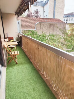 Ein Balkon mit Kunstgr Rasen, einem Holzstuhl und einem Tisch.