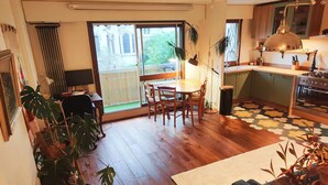 Un coin repas avec une table et des chaises, une cuisine équipée d’une cuisinière et une grande fenêtre donnant sur un immeuble.