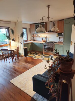 A modern kitchen with a central island, wooden flooring, and a dining area with a table and chairs. - Sunny & Cosy with spectacular balcony view! (Paris)