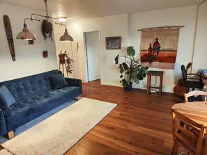 A living room with a blue sofa, wooden flooring, a white rug, a potted plant, a guitar, and a painting on the wall. - Sunny & Cosy with spectacular balcony view! (Paris)
