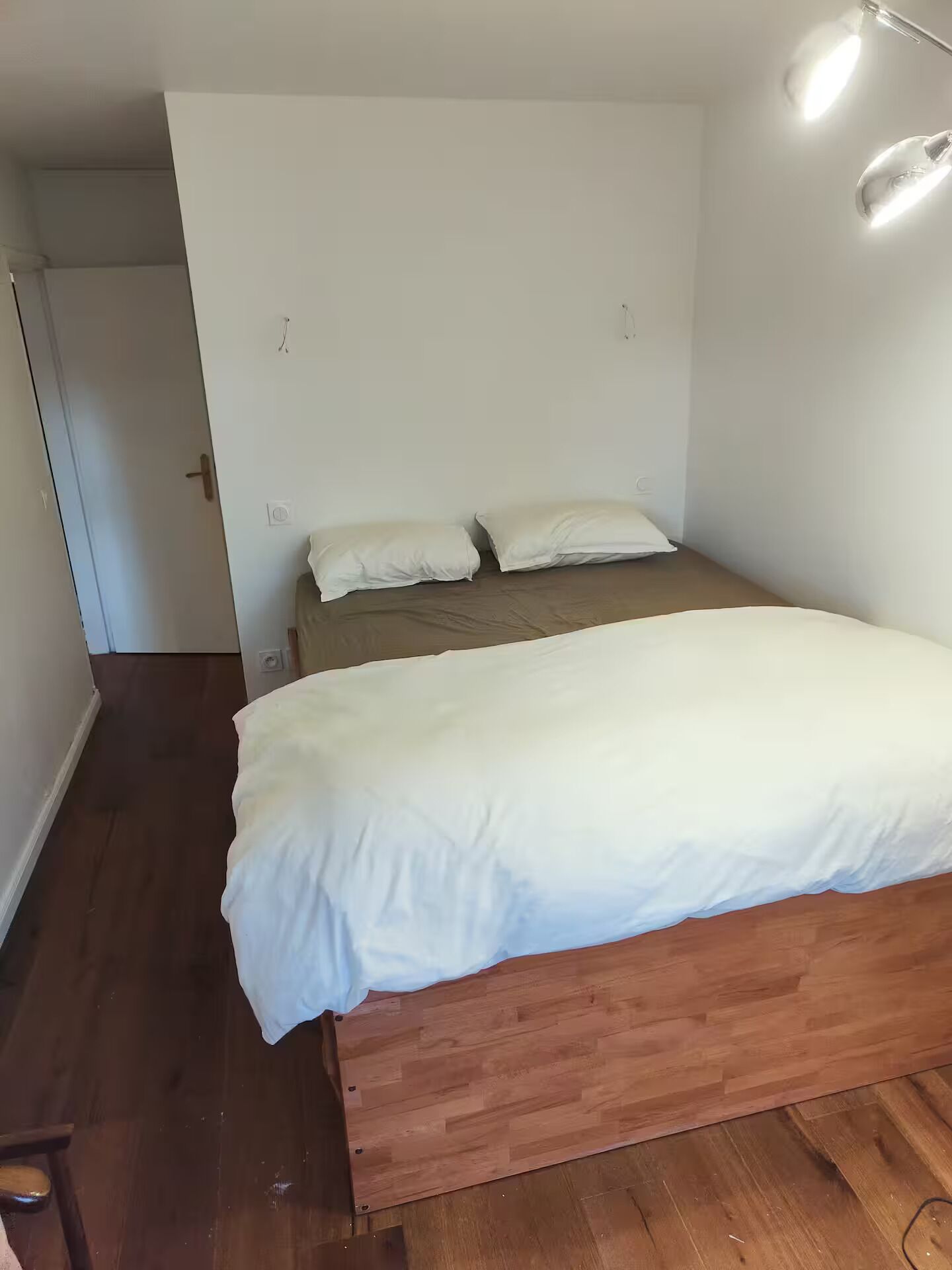 A single bed with a wooden frame and white bedding in a room with white walls and a wooden floor.