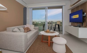 A modern living room with a sofa, a small round table, a TV, and a balcony with a view. - Corporate Stays First Living - 706 (Asunción)