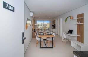Un apartamento moderno con comedor, una computadora portátil sobre un escritorio y un balcón con vistas.
