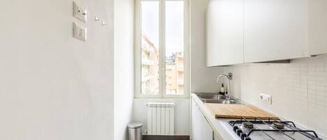 A compact kitchen with a gas stove, white cabinets, a window, and a radiator.