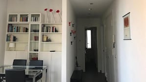 Un interior moderno con una mesa de comedor de vidrio, estanterías blancas y un pasillo que conduce a una puerta.
