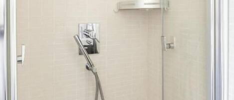 A glass-enclosed shower area with a handheld showerhead and a wall-mounted control panel.