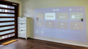 Ein Raum mit einer an der Wand montierten Projektion, die verschiedene App-Symbole zeigt, einem weißen Schrank und einem Holzboden.