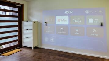A room with a wall-mounted projection displaying various app icons, a white cabinet, and a wooden floor.