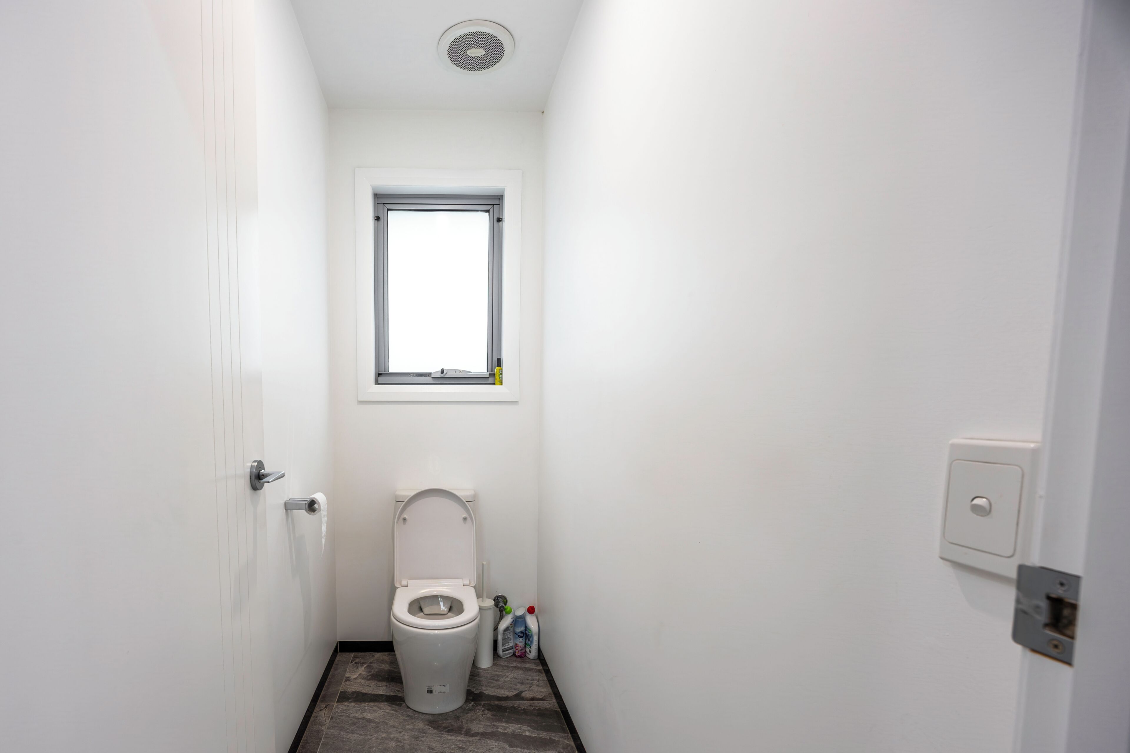 A small, white bathroom with a toilet, a window, and a door.