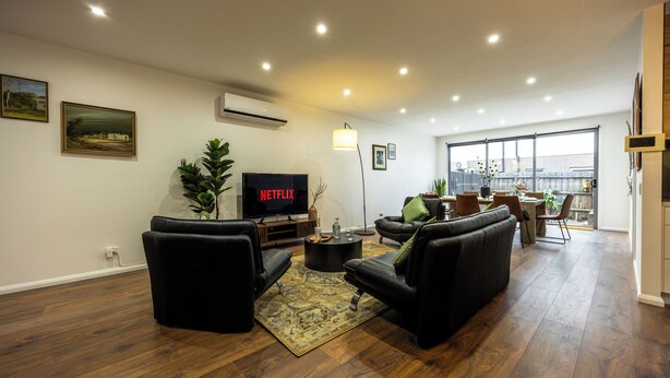 Ein modernes Wohnzimmer mit Flachbildfernseher, Ledersofas, einem Couchtisch und einem großen Fenster.
