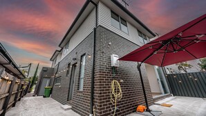 Ein modernes Haus mit Ziegelaußenwand, einem roten Sonnenschirm und einer grünen Mülltonne.