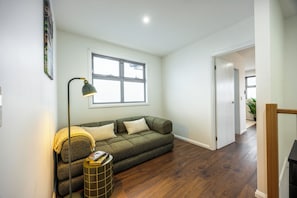 A living room with a sofa, a floor lamp, and a window. - Parkside Ember Luxe w/ Campfire and Entertainment Lounge (Braybrook)
