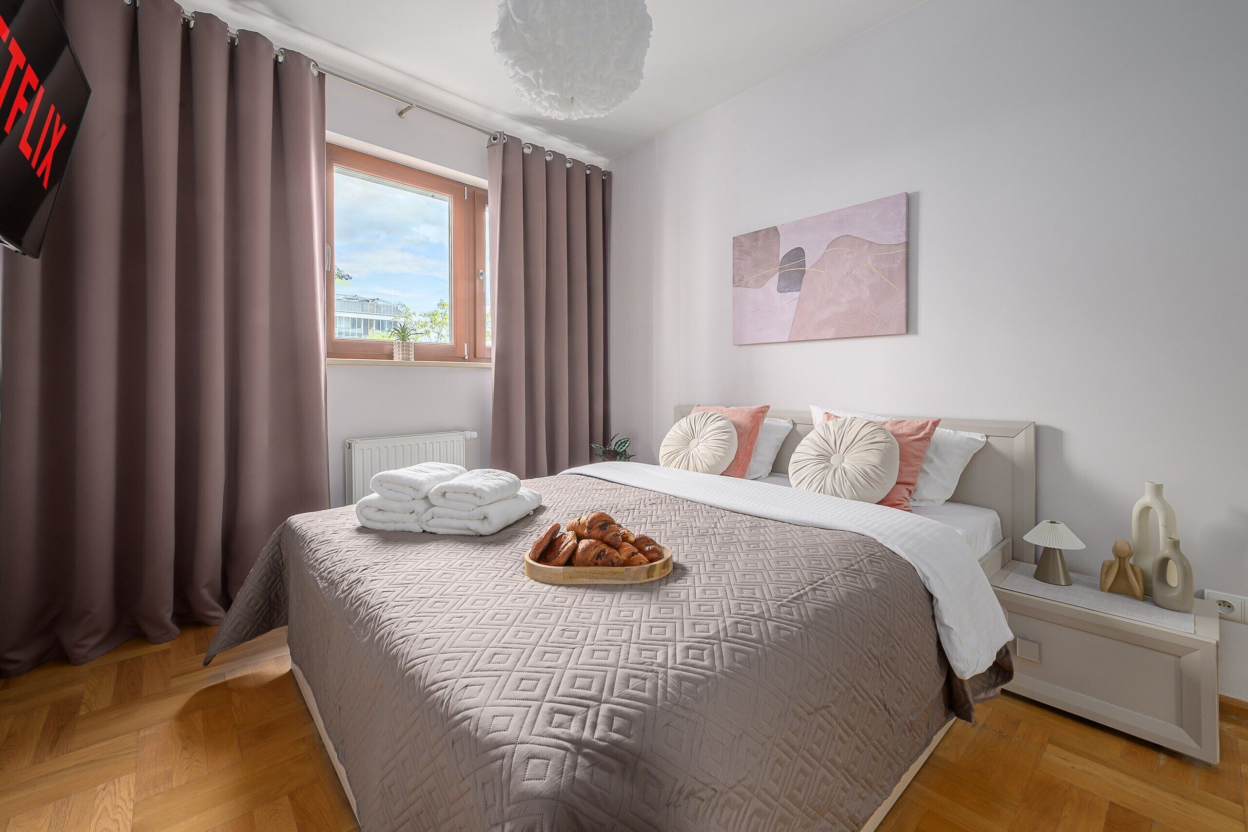 Un dormitorio con cama, ventana, radiador, mesita de noche y una obra de arte en la pared.