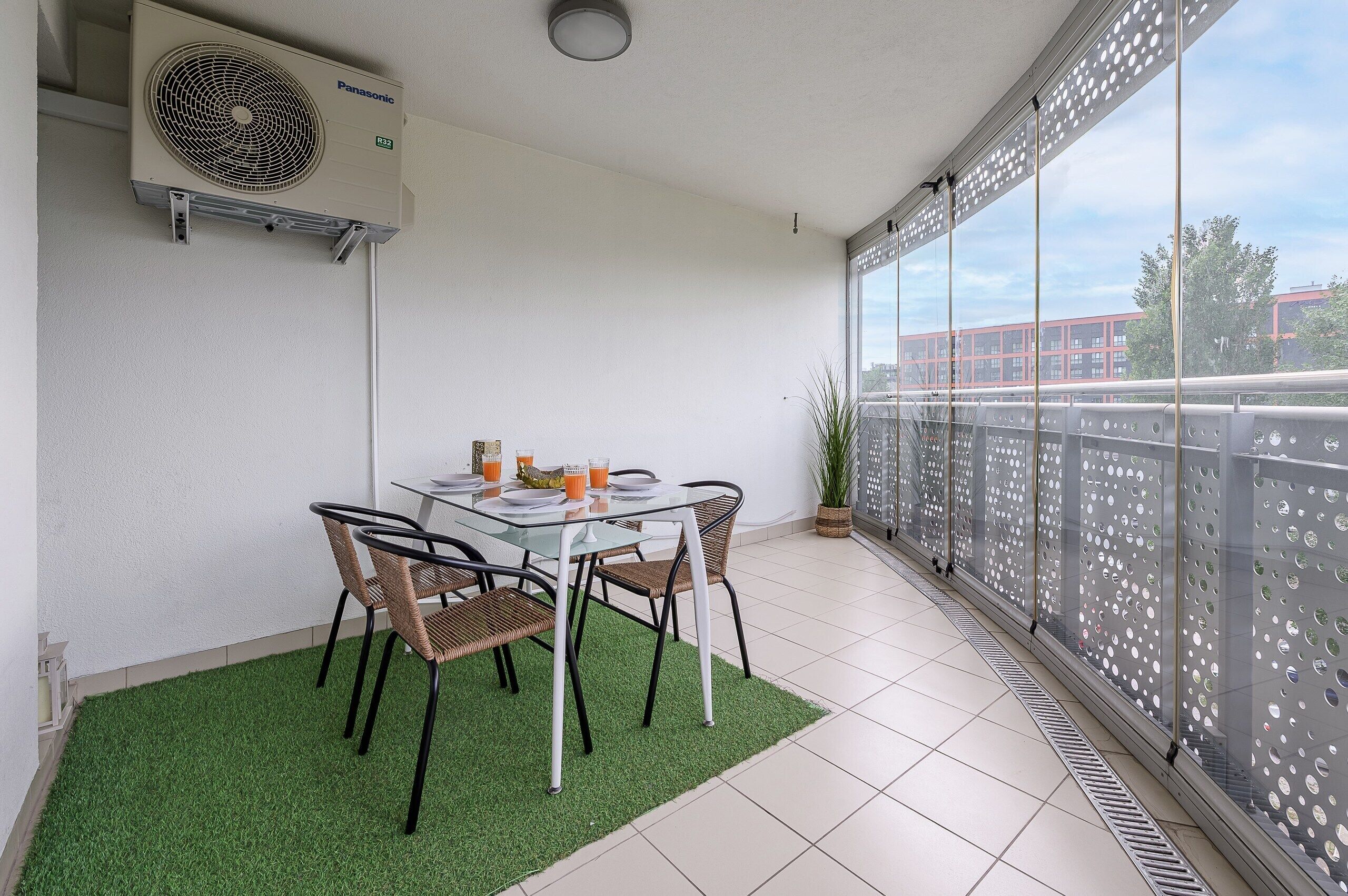 Un balcón con una mesa, sillas, una planta en maceta y vistas a un edificio.