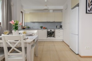 A modern kitchen with white cabinetry, a Bosch oven, and a dining area with a white table and chairs. - Lumina 3-room Apart with Parking  (Warszawa)