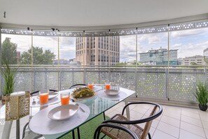 Ein Balkon mit Glastisch, Stühlen und Blick auf Stadtgebäude.