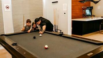 A pool table in a room with a closed door, a coffee machine, and a hanging light fixture.
