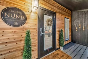 Fachada de madera con una puerta negra, felpudo y un letrero que dice 'Comfortably NUMB Fredericksburg, TX'.