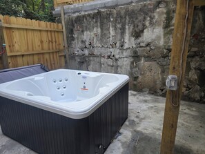 A hot tub in an outdoor setting with a wooden fence, stone wall, and electrical outlet. - Over-The-Rhine 4-bedroom 3 bathroom house with off street parking in Cincinnati (Cincinnati)