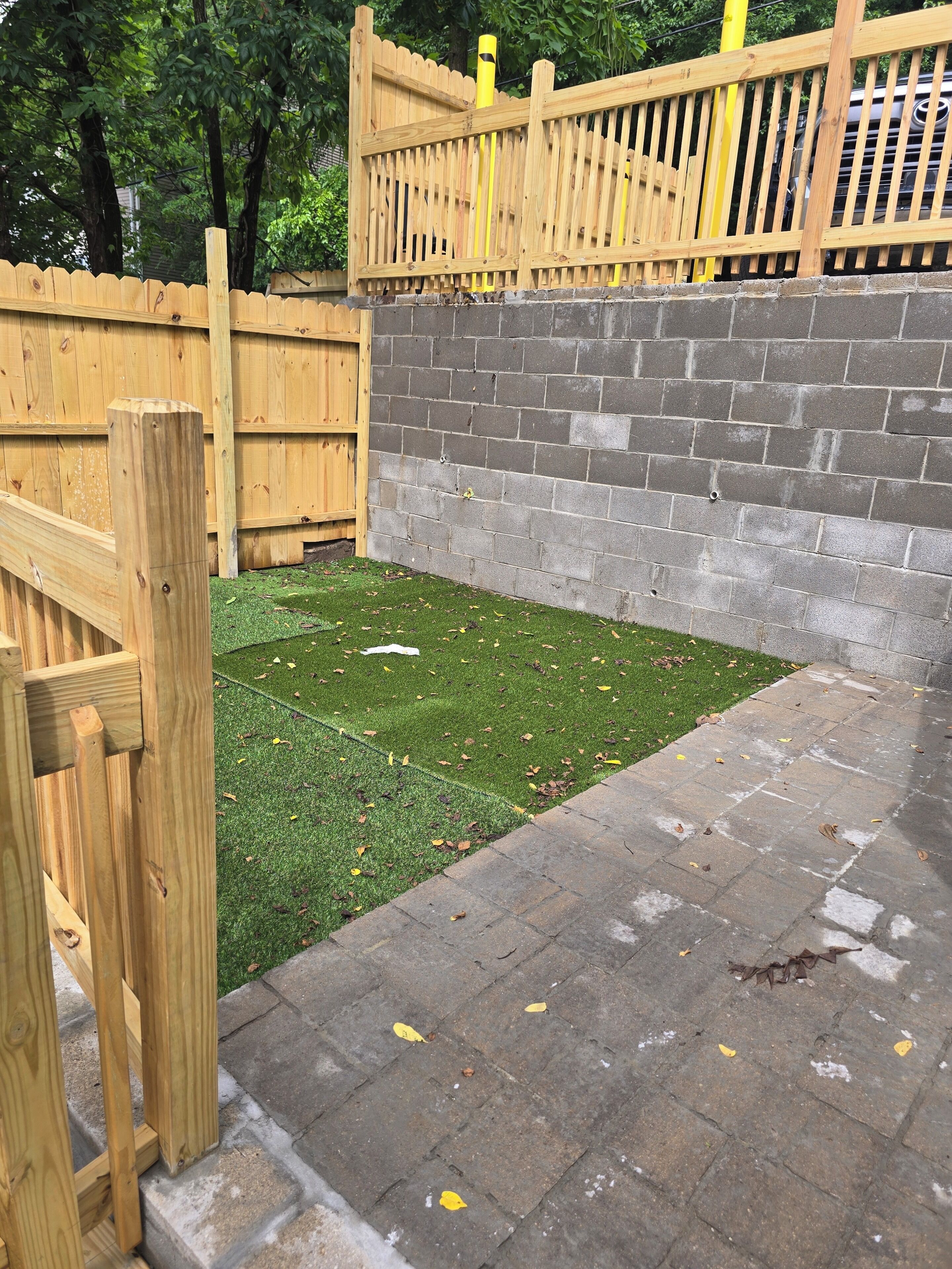 A fenced outdoor area with artificial grass and a paved walkway.