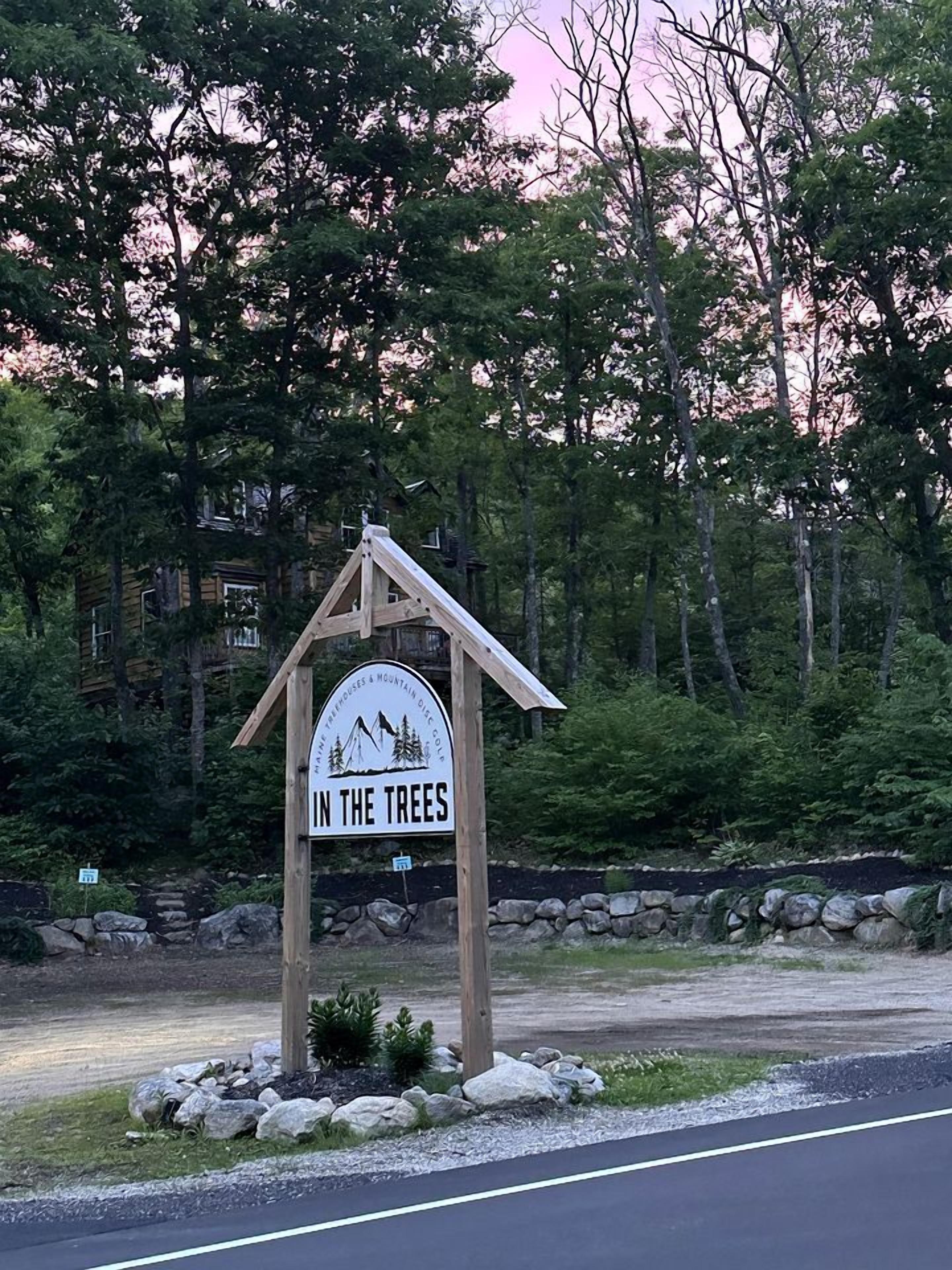 A wooden sign with the text 'IN THE TREES' and a mountain and tree illustration.