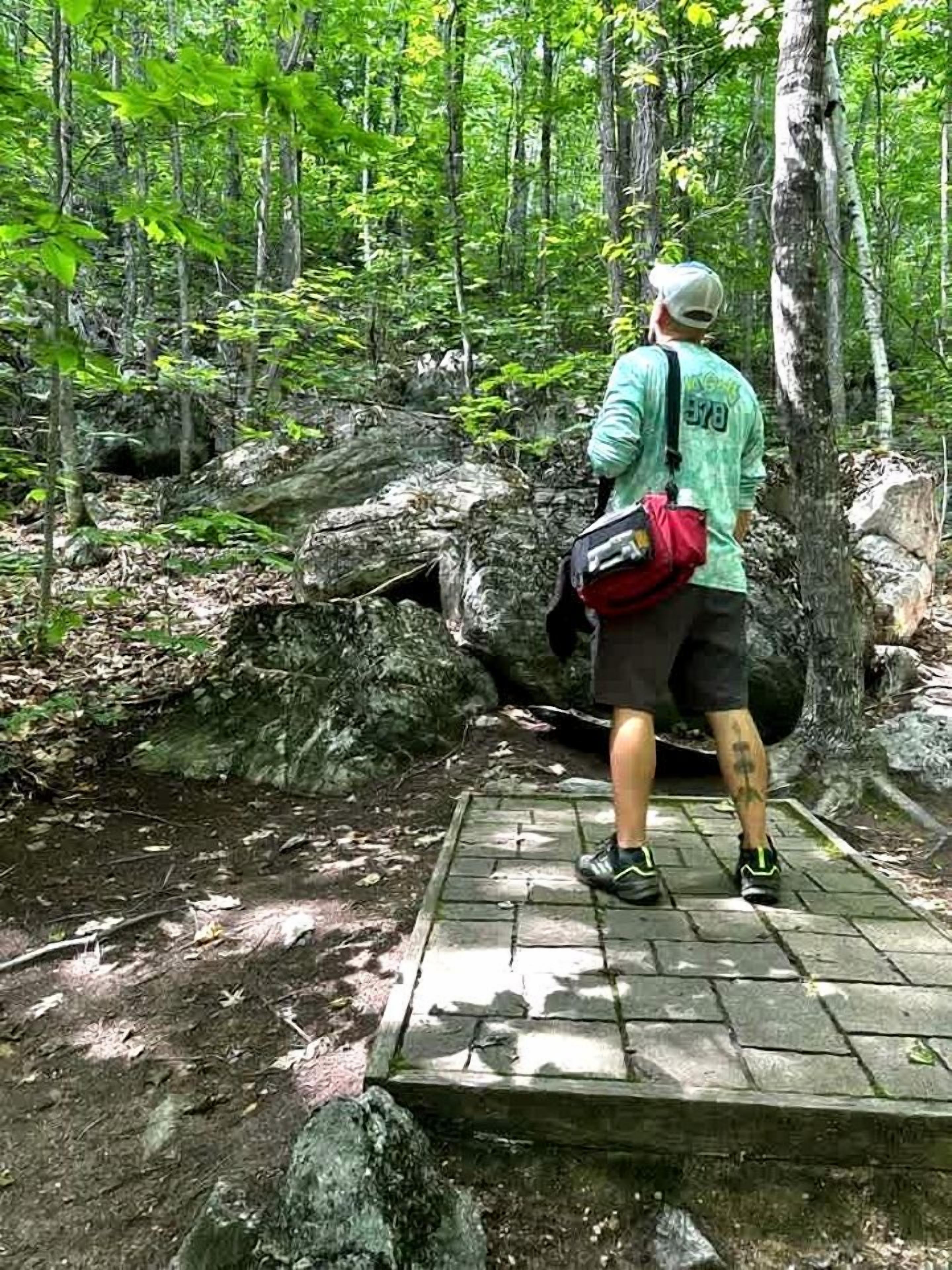 A person standing on a stone platform in a forested area with trees and rocks.