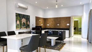 Ein stilvolles Wohnzimmer mit Marmorboden, einem Essbereich mit weißem Tisch und Stühlen, einer schwarzen Couch mit floralen Kissen und einem großen Gemälde an der Wand.