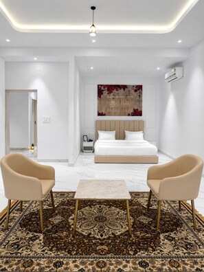 Ein modernes Schlafzimmer mit einem großen Bett, zwei Sesseln, einem gemusterten Teppich und einer Wanddekoration.