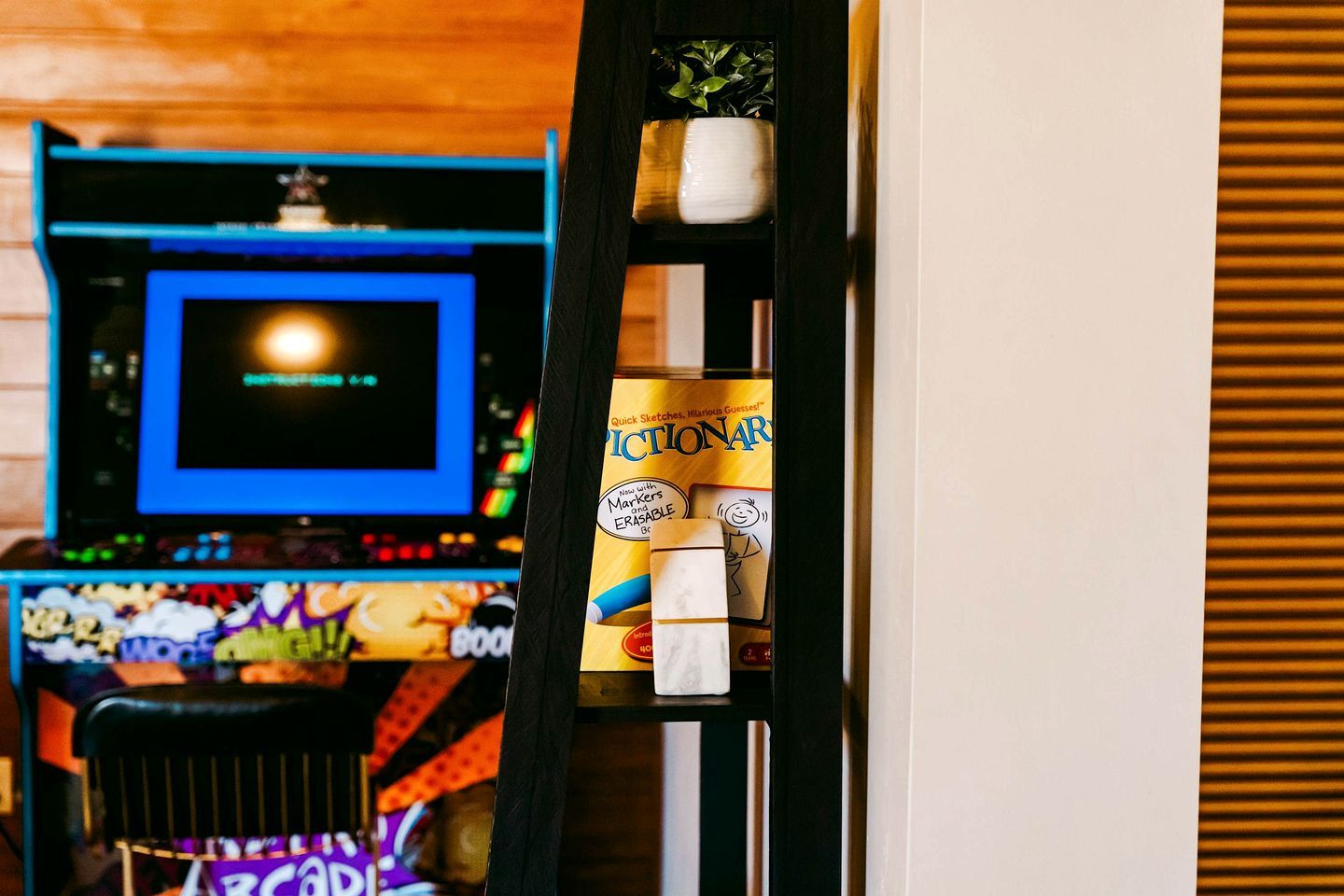 Una habitación con una consola de videojuegos, una silla y una estantería con una caja etiquetada 'Picton'.