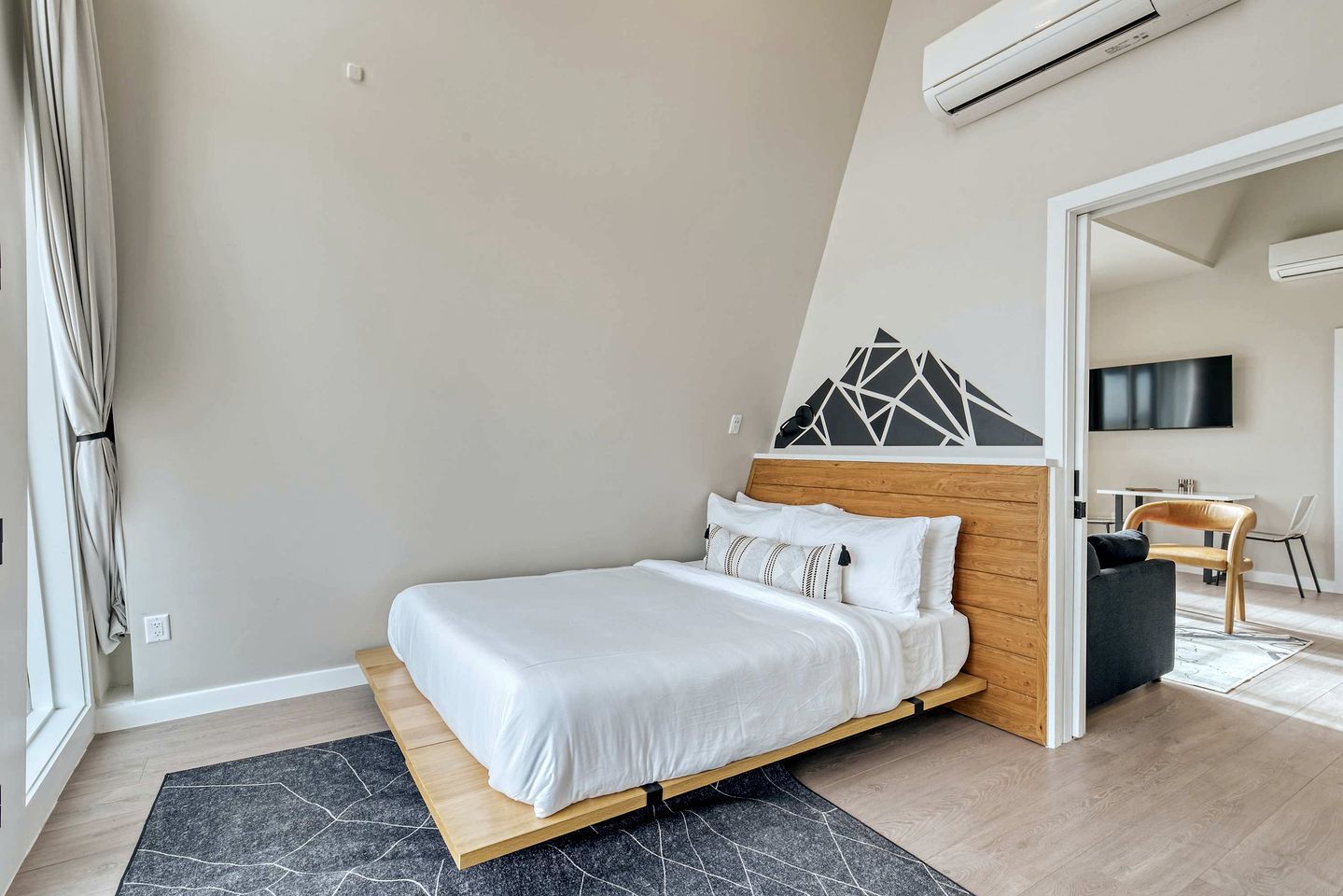 A modern bedroom with a bed, a geometric wall decoration, a TV, and a dining area.