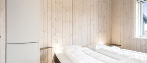 A bedroom with two beds, wooden walls, a wardrobe, bedside lamps, and a window.