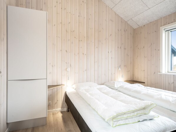 A bedroom with two beds, wooden walls, a wardrobe, bedside lamps, and a window.